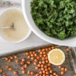 Chopped lettuce in a large serving bowl next to a small bowl of salad dressing, and a baking tray of roasted chickpeas.