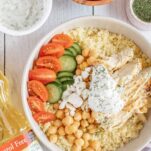 Couscous bowl topped with chicken, chickpeas, veggies, and Greek dressing.