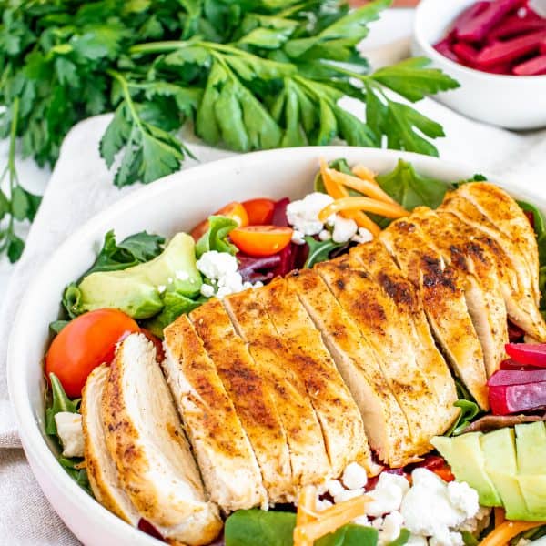 Grilled Chicken sliced and laying on a freshly made salad in a white serving bowl.