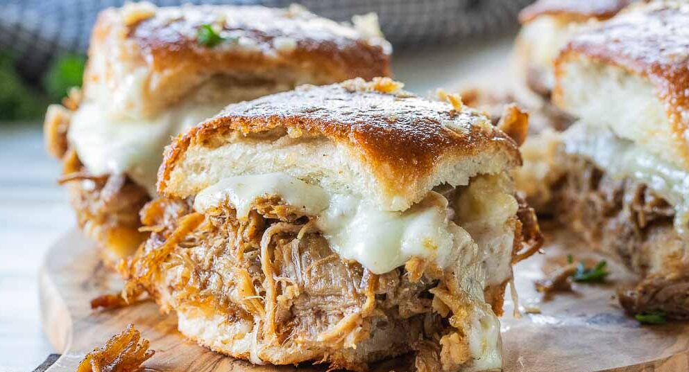 pulled pork sliders with melted cheese oozing out on a wooding tray