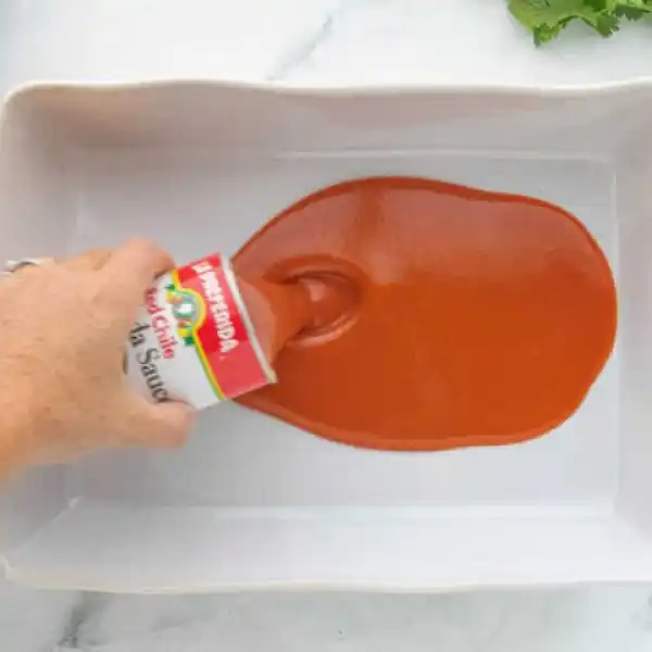 enchilada sauce being poured into a baking pan
