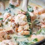 tuscan shrimp shown in a skillet with a wooden spoon