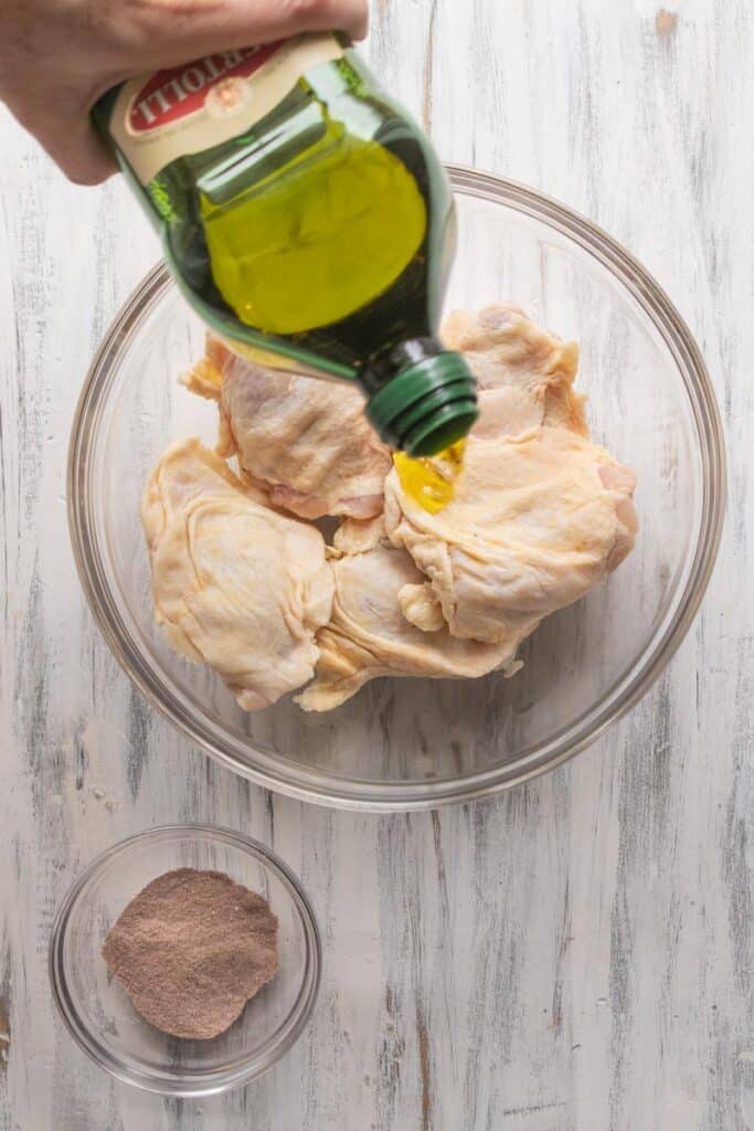 chicken thighs with olive oil being added in a bowl