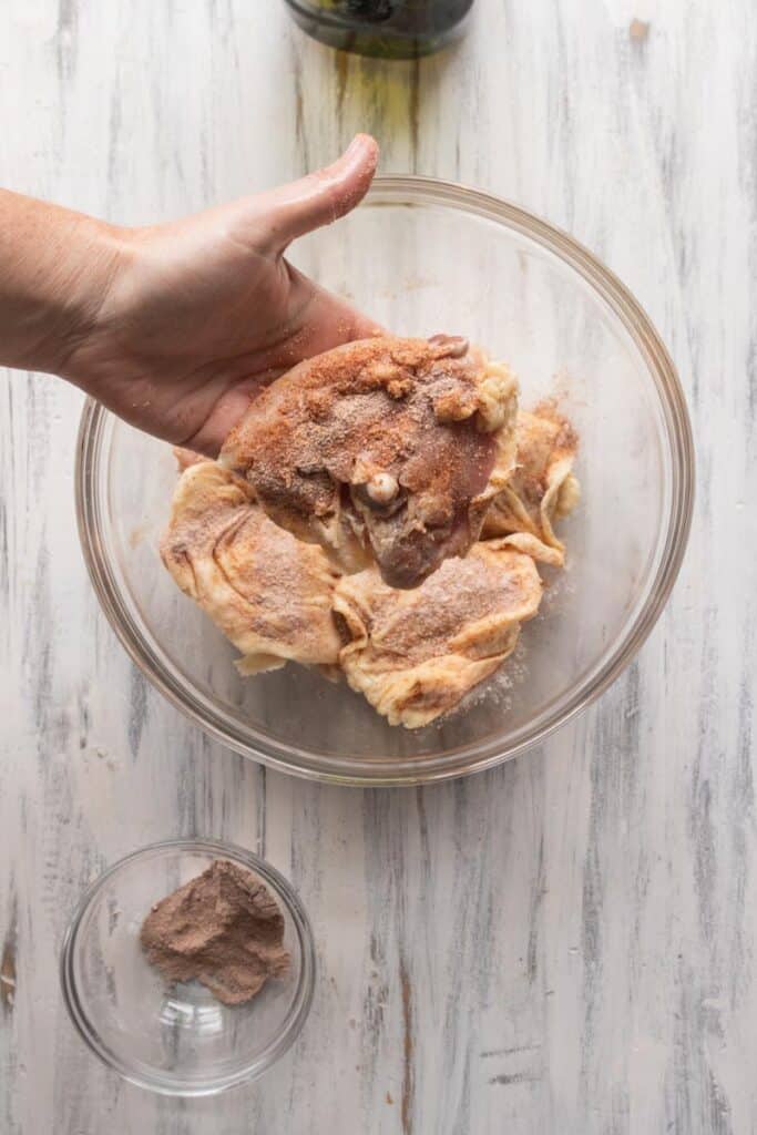 chicken thighs getting seasoned in a bowl